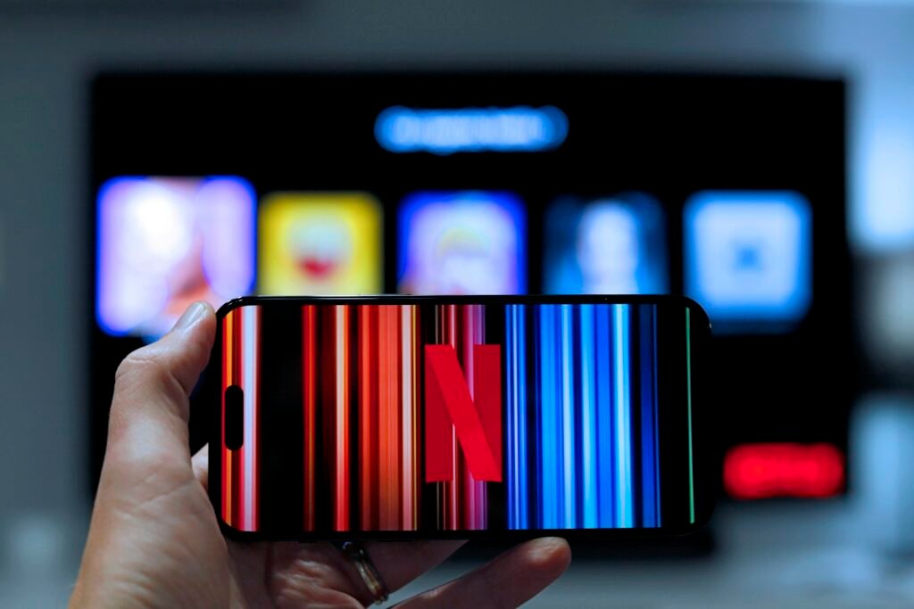 Netflix on a smartphone in front of a television showing profile selection