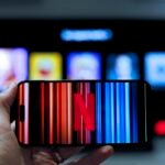 Netflix on a smartphone in front of a television showing profile selection